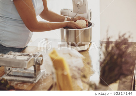 Women's hands take out dough from the dough mixer to make noodles in a noodle cutter 90217144
