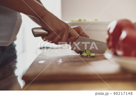 Cutting vegetables with a knife on a wooden board in the background of the kitchen 90217148