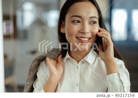 Close up of smiling asian business woman making phone call standing at office 90217159