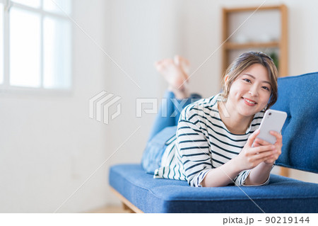 ソファーでスマホを操作する若い女性 90219144