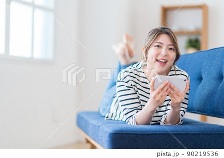 ソファーでスマホを操作する若い女性。 ソファーでスマホを操作する若い女性。 90219536
