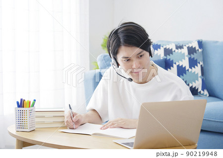 リビングでヘッドセットをつけてパソコンを見て勉強する男性 90219948