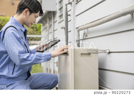 住宅の屋外に設置されたガス給湯器の点検をする作業服の男性 住宅の屋外に設置されたガス給湯器の点検をする作業服の男性 90220273