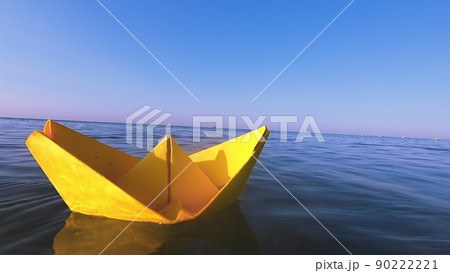 Yellow paper boat floats on surface of blue water waves of sea close-up. Clear blue sky on sunny summer day. Concept adventures travelling vacation holiday rest tourism voyager dream. Slow motion 90222221