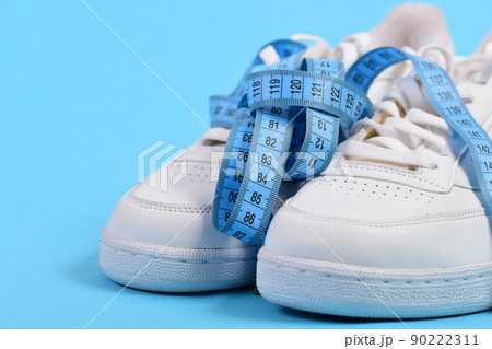 Sport shoes and blue measuring tape on cyan background. 90222311