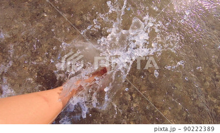 Girl with bare feet walking on water on sandy beach of sea and splashes water her feet on summer sunny day. Barefoot on sand beach. Vacation enjoyment rest relax travel tourism holiday. Slow motion 90222389