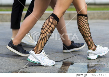 Three pairs of slim fit young girls legs in different sport shoes walking fast along the concrete road.Busy city lifestyle. Three pairs of slim fit young girls legs in different sport shoes walking fast along the concrete road.Busy city lifestyle. 90224458