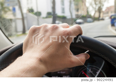 Steerind wheel with driver hand on it in modern car interior with view of street 90224491