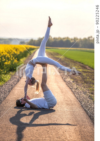 Beautiful young couple doing acro yoga on the bike path. Man lying on road and balancing woman in his feet. Beautiful young couple doing acro yoga on the bike path. Man lying on road and balancing woman in his feet. 90225246