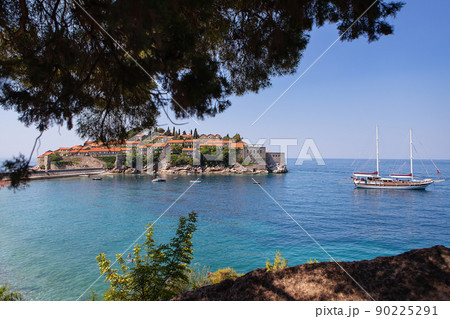 Famous architectural monument of the island resort of St. Stephen St. Stephen in the Adriatic Sea, Montenegro. The concept of vacation at sea, boat in the sea. Photo through the trees. 90225291
