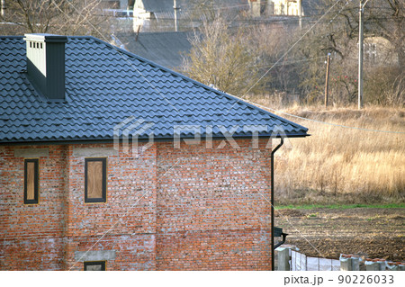 Brick house with roof top covered with metallic shingles. Tiled covering of building under construction Brick house with roof top covered with metallic shingles. Tiled covering of building under construction 90226033