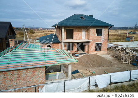 Aerial view of unfinished house with brick walls and wooden roof frame covered with metallic tiles under construction 90226359