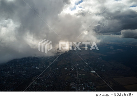 Aerial view from airplane window at high altitude of distant city covered with white puffy cumulus clouds Aerial view from airplane window at high altitude of distant city covered with white puffy cumulus clouds 90226897