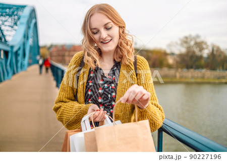 Smiling beautiful woman carrying eco paper shopping bags on the bridge in the city Smiling beautiful woman carrying eco paper shopping bags on the bridge in the city 90227196