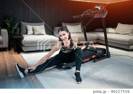 cheerful female stretching and preparing for cardio workout on treadmill at home 90227556