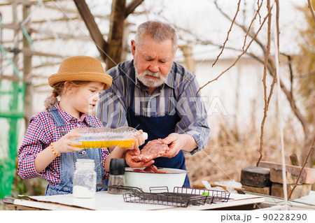 granddaughter helps grandfather cook barbecue and pours sunflower oil on meat granddaughter helps grandfather cook barbecue and pours sunflower oil on meat 90228290