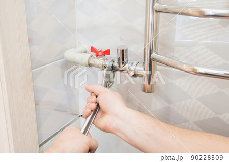 A male plumber repairs the pipes of the heated towel rail in the bathroom. A male plumber repairs the pipes of the heated towel rail in the bathroom. 90228309
