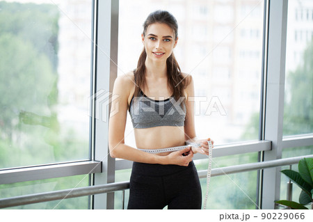 Sporty young woman measuring her waist in the fitness studio 90229066