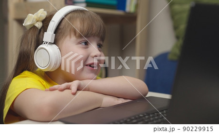 little schoolgirl headphones does homework while sitting digital laptop. distance learning online students. children funny communication through internet video communication. lessons monitor display. 90229915