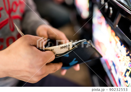 パチンコ屋で財布から1万円札を投資する様子 90232553