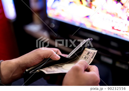 パチンコ屋で財布から1万円札を投資する様子 パチンコ屋で財布から1万円札を投資する様子 90232556