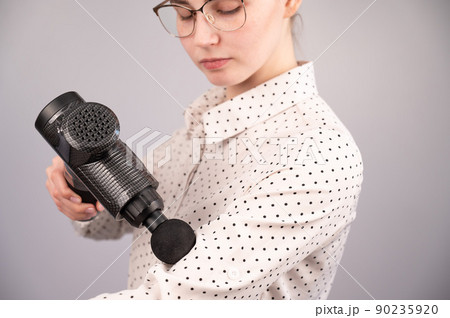 Caucasian business woman massaging her biceps with a percussion massager. 90235920