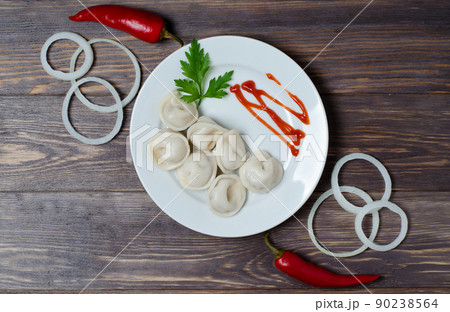 Traditional Russian dumplings, ravioli, dumplings on a white plate with red sauce and parsley. Dark wooden background. Onion rings, chili. 90238564
