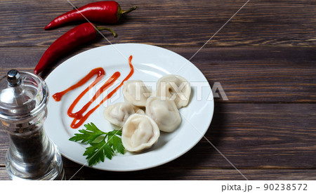 Traditional Russian dumplings, ravioli, pelmeni on a white plate with red sauce and parsley. Dark wooden background. Top view. Copy space Traditional Russian dumplings, ravioli, pelmeni on a white plate with red sauce and parsley. Dark wooden background. Top view. Copy space 90238572