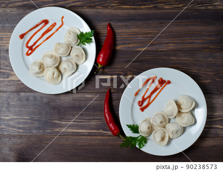 Traditional Russian pelmeni, ravioli, dumplings on a white plate with red sauce and parsley. Dark wooden background. Traditional Russian pelmeni, ravioli, dumplings on a white plate with red sauce and parsley. Dark wooden background. 90238573
