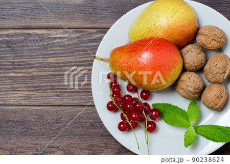 Vegetarian food. Ripe pears, walnuts, red currant, mint leaves on a white round plate. Flat top view 90238624