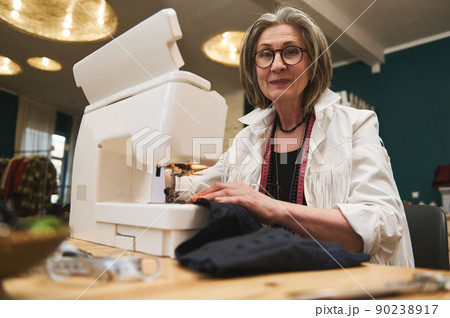 Mature woman sewer in workshop studio, works on sewing machine, designing new collection clothes. Fashion designer business start-up, entrepreneur concept 90238917