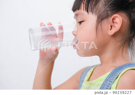 Cute little girl drinking milk from a glass isolated on white background. Little girls enjoy drinking milk before going to school. Cute little girl drinking milk from a glass isolated on white background. Little girls enjoy drinking milk before going to school. 90239227