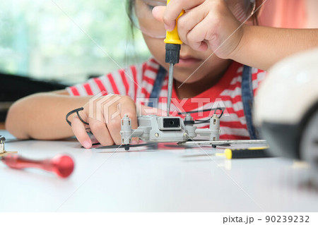 Concentrated little girl repairing her toy drone with a tool in hand and carefully assembles toy drone with screwdriver. STEM Hobbies for advanced smart kids. Concentrated little girl repairing her toy drone with a tool in hand and carefully assembles toy drone with screwdriver. STEM Hobbies for advanced smart kids. 90239232