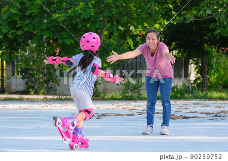 Asian mother helps daughter practice roller skating in the park. Exciting outdoor activities for kids. 90239752