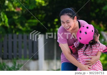 Asian mother helps daughter practice roller skating in the park. Exciting outdoor activities for kids. 90239753