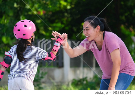 Asian mother helps daughter practice roller skating in the park. Exciting outdoor activities for kids. 90239754