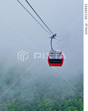 Bright red cable car with double safety sling to the cloudy misty forest in highland mountain in rainy day 90239893
