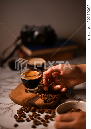 A female hand holding a glass of espresso shot. close-up image, dark coffee, espresso shot 90240005