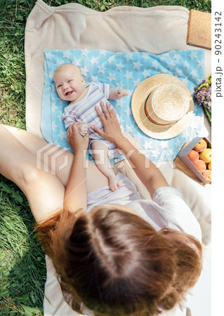 Newborn baby spending time outside. Happy and smiling mother with her newborn baby spending time in the park. Getting fresh air and natural sunlight for babies. Newborn baby spending time outside. Happy and smiling mother with her newborn baby spending time in the park. Getting fresh air and natural sunlight for babies. 90243142
