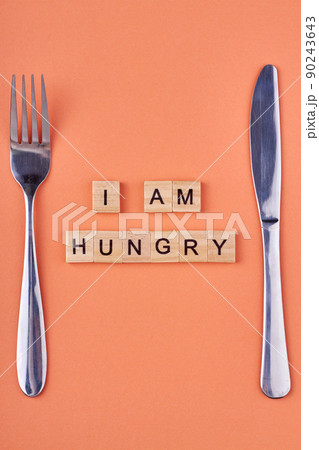 I am hungry inscription on wooden blocks. Fork and knife on table. 90243643
