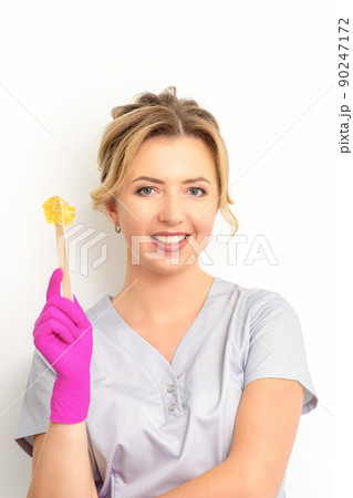The master of sugar hair removal holds liquid yellow sugar paste, wax for depilation on a wooden stick on a white background 90247172