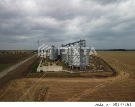 Grain elevator. Metal grain elevator in agricultural zone. Agriculture storage for harvest. Grain elevators on green nature background. Exterior of agricultural factory. Nobody. Grain elevator. Metal grain elevator in agricultural zone. Agriculture storage for harvest. Grain elevators on green nature background. Exterior of agricultural factory. Nobody. 90247261