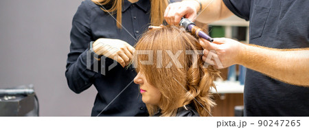Two hairstylists make curls hairstyle of long brown hair with the curling iron in hairdresser salon Two hairstylists make curls hairstyle of long brown hair with the curling iron in hairdresser salon 90247265