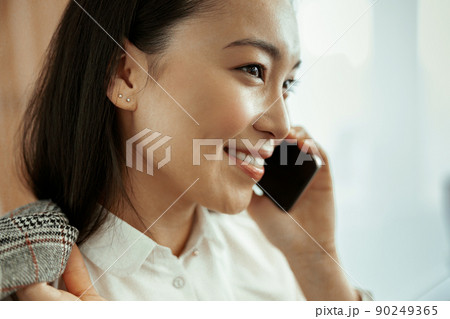 Close up of smiling asian business woman making phone call standing at office 90249365