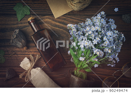 Tincture or potion bottle, sachet of dried herbs, glasses, bouquet of wild forget me not flowers. Top view, flat lay. 90249474