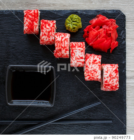 Sushi roll with seafood and soy sauce, wasabi and ginger. Sushi roll with caviar on a black board. 90249773