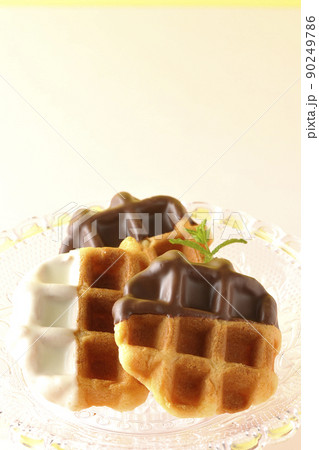 透明なガラス製のケーキスタンドに盛り付けられているチョコがコーティングされたワッフル 透明なガラス製のケーキスタンドに盛り付けられているチョコがコーティングされたワッフル 90249786