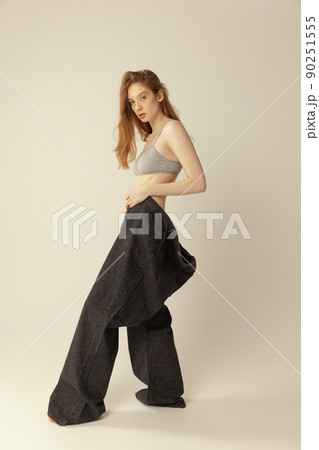 Portrait of young slim girl in top and giant black jeans posing isolated over grey studio background. Weight-loss concept 90251555