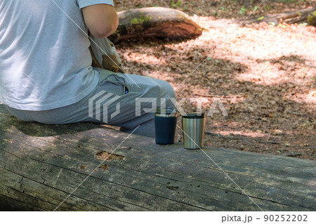 Traveler food for outdoor activities. Two metal thermo cups on a forest background. Enjoy a coffee during trips. Traveler food for outdoor activities. Two metal thermo cups on a forest background. Enjoy a coffee during trips. 90252202