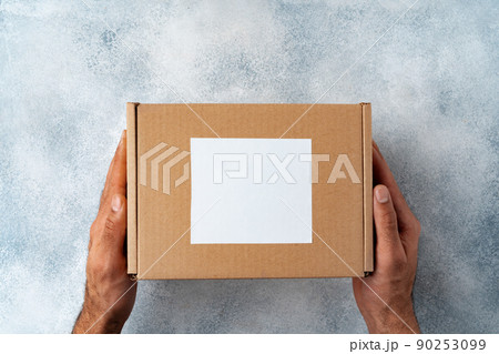 Parcel cardboard box in a man hands on a gray table background Parcel cardboard box in a man hands on a gray table background 90253099